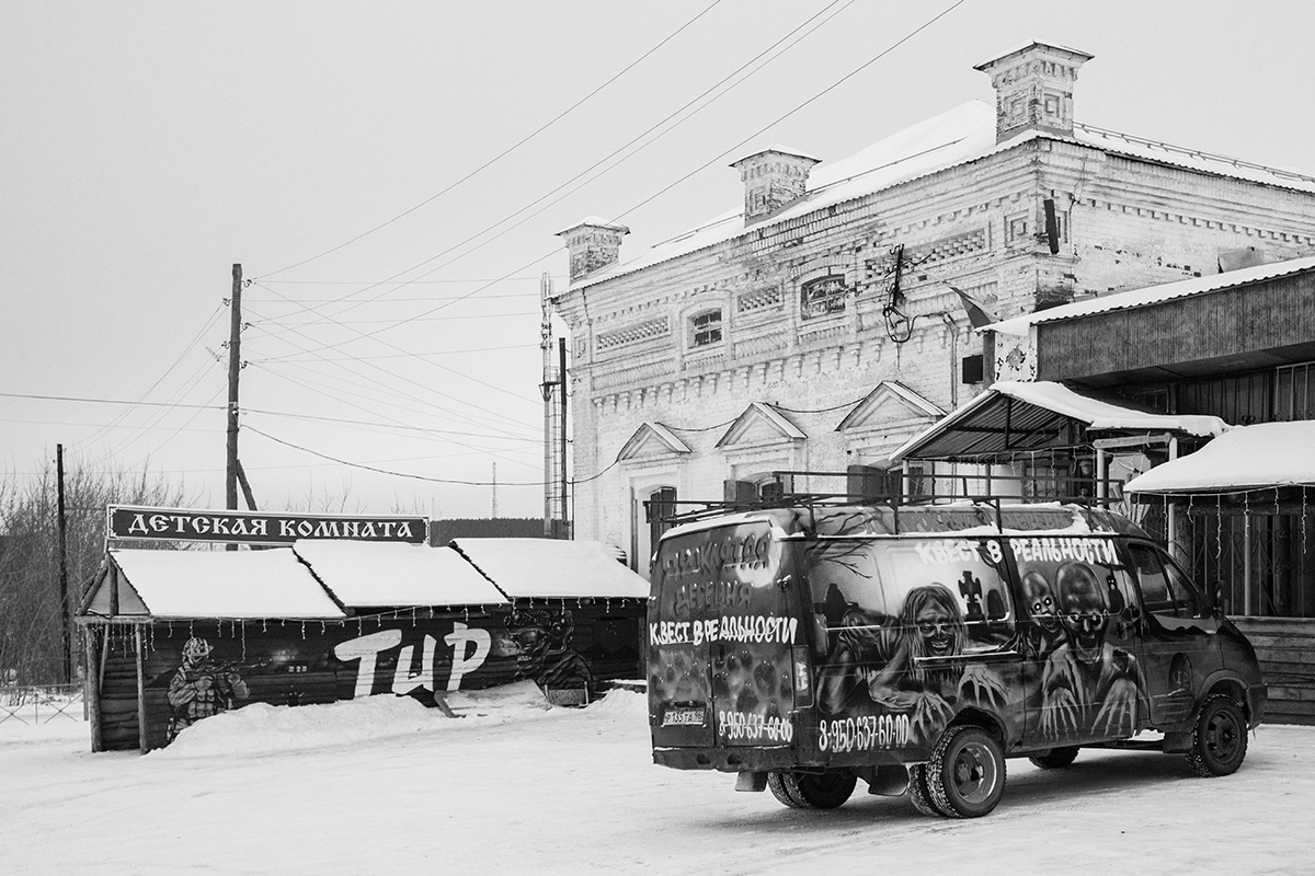 Чёрно-белая фотография заброшенного здания и ярко разрисованного фургона на фоне снега. Сысерть, Россия, 2024.