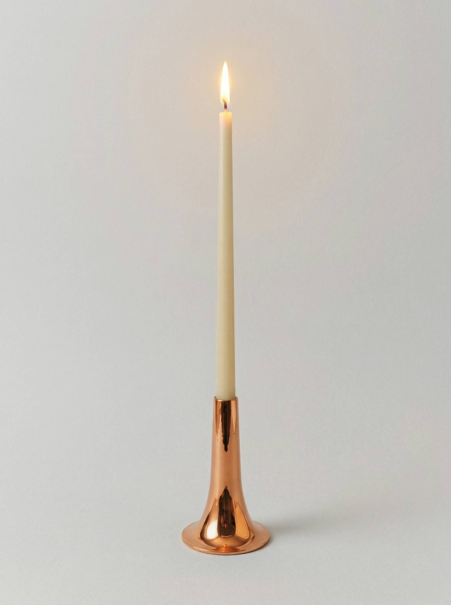 Высокий узкий подсвечник из меди с установленной свечой, создающий теплое мягкое освещение