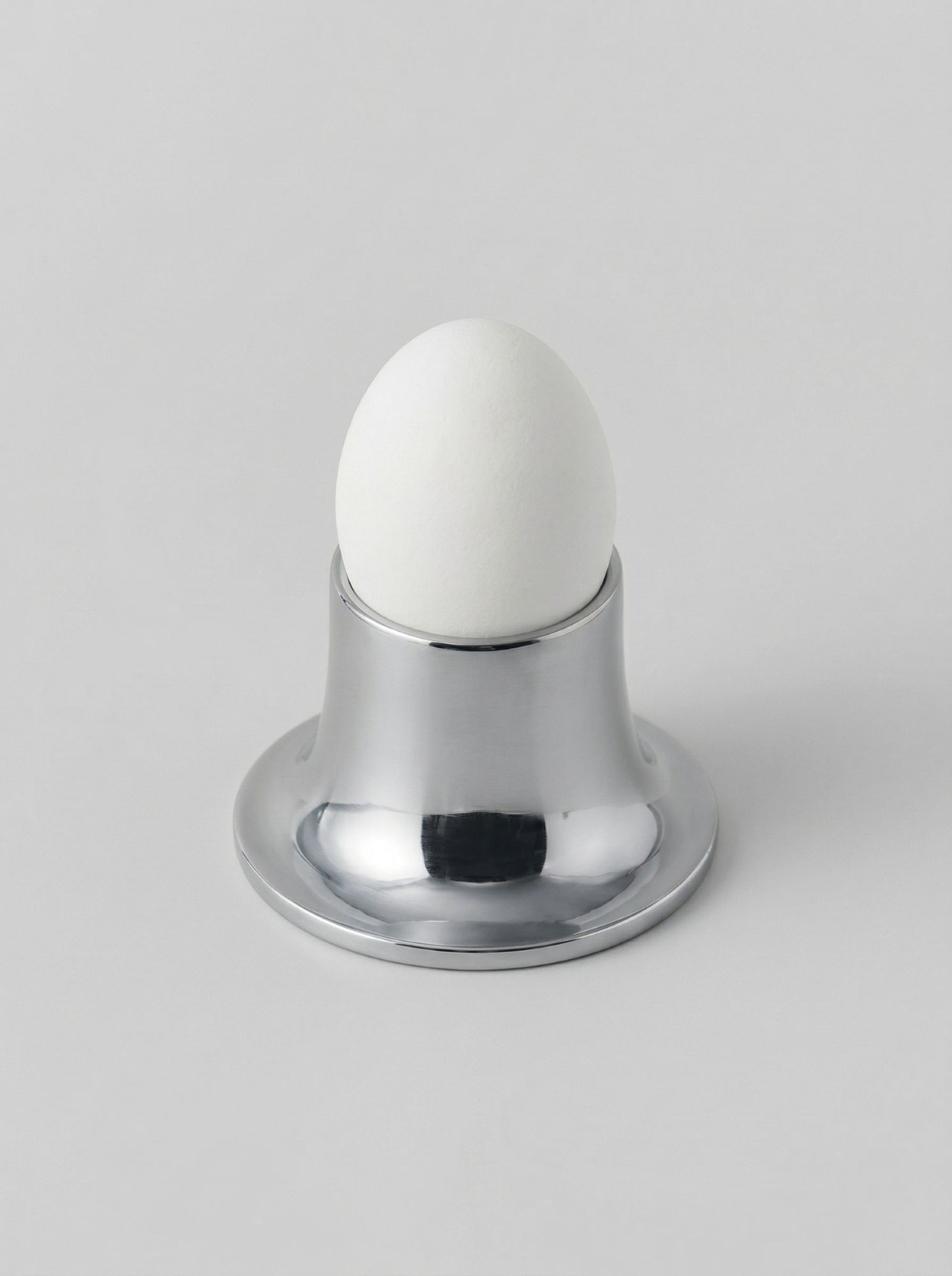 Металлическая подставка серебристого оттенка с яйцом, минималистичный дизайн на нейтральном фоне